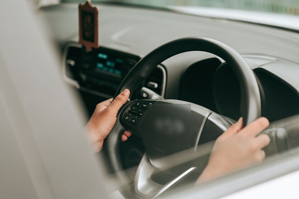 Dua tangan memegang setir mobil di kabin yang terang pada siang hari.