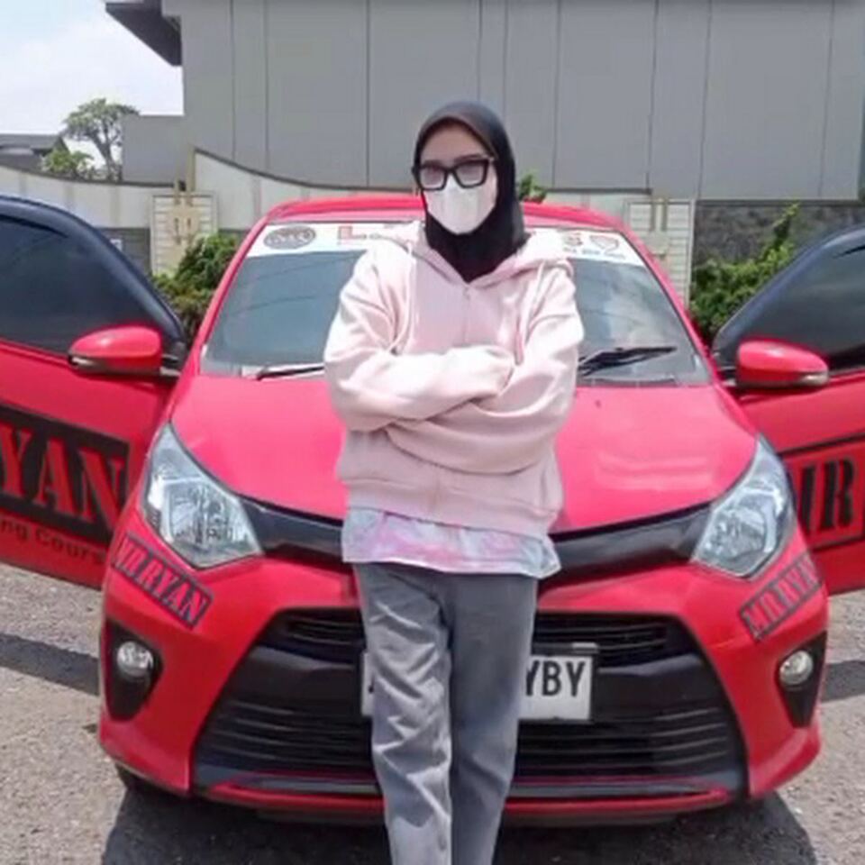 Seorang siswi berdiri di depan mobil merah MR RYAN.
