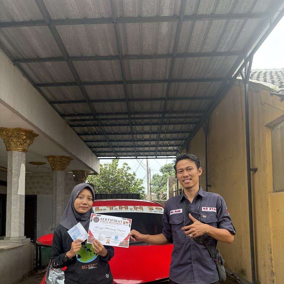 Seorang siswi memegang sertifikat kursus bersama instruktur di depan mobil MR RYAN.