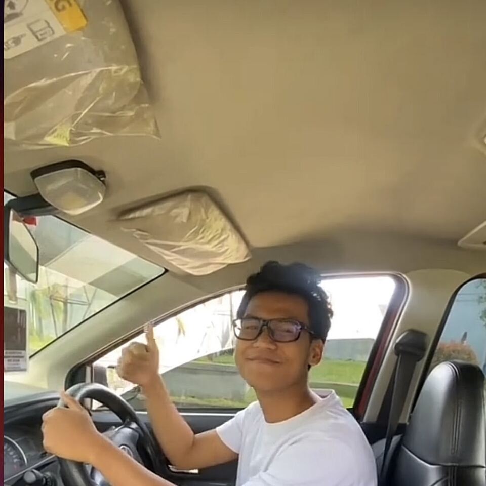 Seorang siswa duduk di kursi pengemudi mobil sambil mengacungkan jempol.