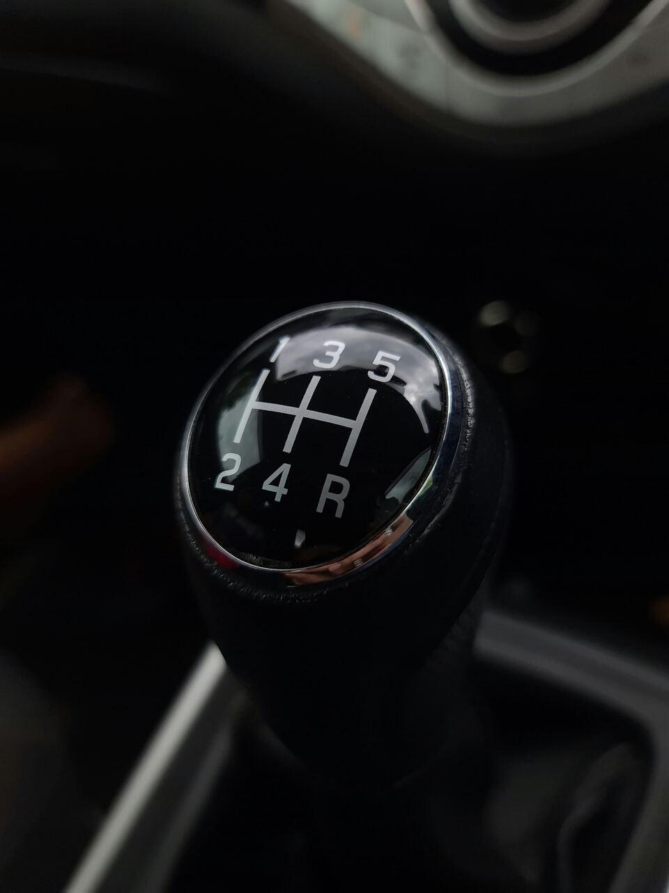 Close-up tuas transmisi manual dengan pola gigi satu sampai lima dan mundur di kabin mobil.